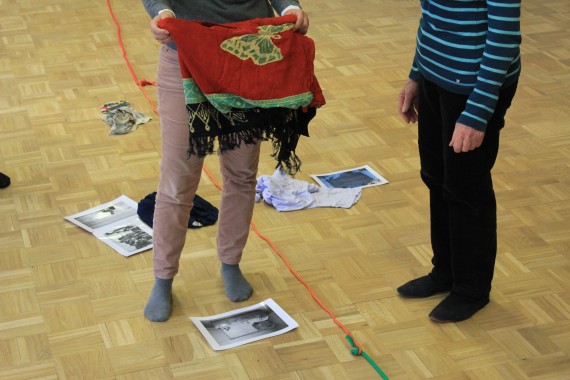 Auf Holzboden verläuft Schnur; an einigen Stellen entlang der Schnur liegen Fotos und Objekte  