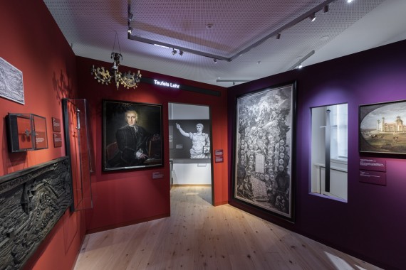 Ausstellungsraum &quot;Macht und Ohmacht&quot; mit Kronleuchter und historischen Gemälden an den dunkelrot und lila gestrichenen Wänden