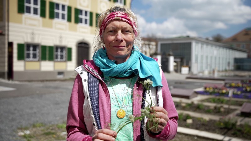 Frau im Kräutergarten vor gelbem Begäude mit grünen Fensterläden (Kempten-Museum)