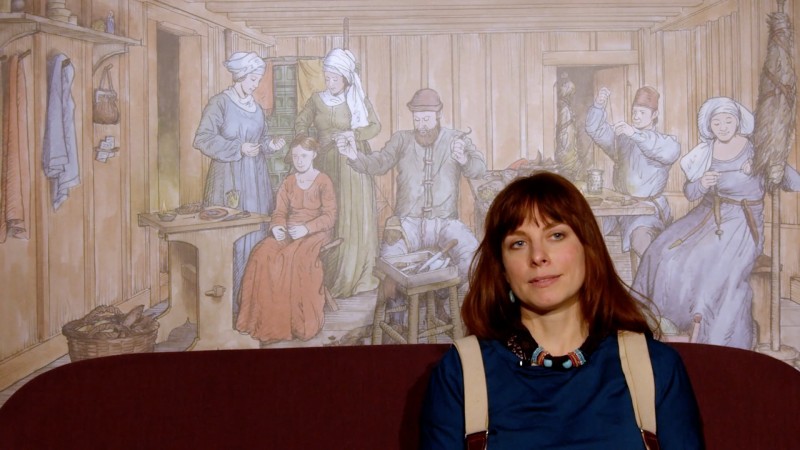 Laura Kral vor Gemälde, das eine mittelalterliche Wohnstube zeigt
