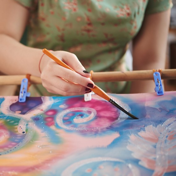 Mädchen bemalt ein Seidentuch mit bunten Farben und kreisförmigen Mustern