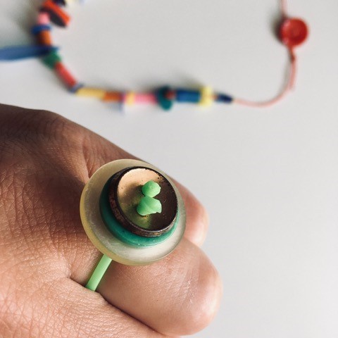 Hand mit DIY-Ring aus gr&uuml;nem Gummiband und Kn&ouml;pfen in Gr&uuml;nt&ouml;nen und Gold