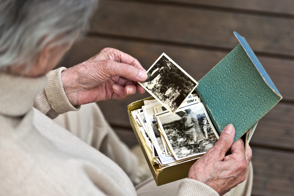 Alte Frau von hinten sitzend betrachtet ein schwarz-weiß Foto, hält Fotokästchen mit weitern Bildern in der Hand