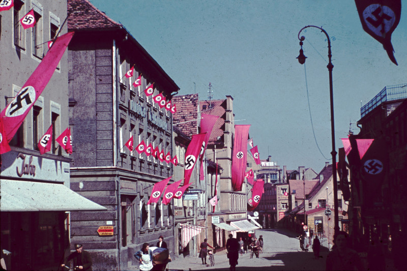 Fußgängerzone, Fischerstraße in der Kemptener Innenstadt, an den Fenstern und Hausfassaden sehr viele roten NS-Fahnen (mit weißem Kreis, in dem ein Hakenkreuz abgebildet ist)