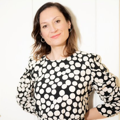 lächelnde junge Frau mit halblangen braunen Haaren und schwarz-weiß gepunktetem Kleid