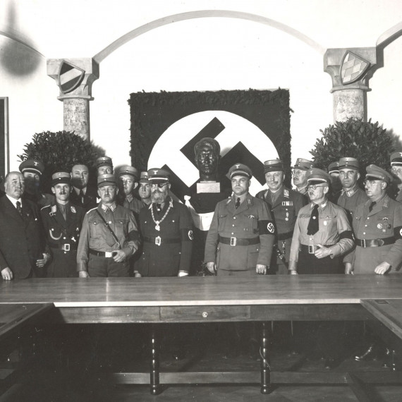 Männer in Uniformen stehen vor einem Hakenkreuz