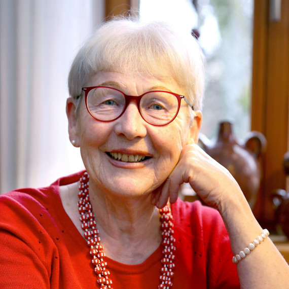 lachende Frau mit rot umrandeter Brille und rotem Shirt, sie stützt den Kopf in die Hand