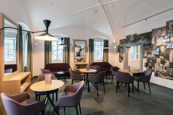 Museum café: round wooden tables with modern armchairs in the color purple. On the wall: pictures of Kempten personalities.