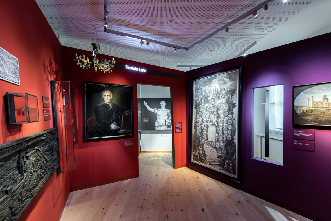 Exhibition space &quot;The Powerfull and the Powerless&quot; with chandelier and historical paintings on the dark red and purple painted walls