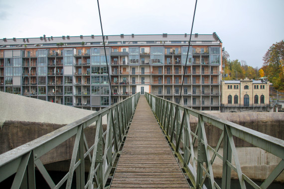 eine Brücke mit Stahlgeländer führt auf einen Wohnblock zu