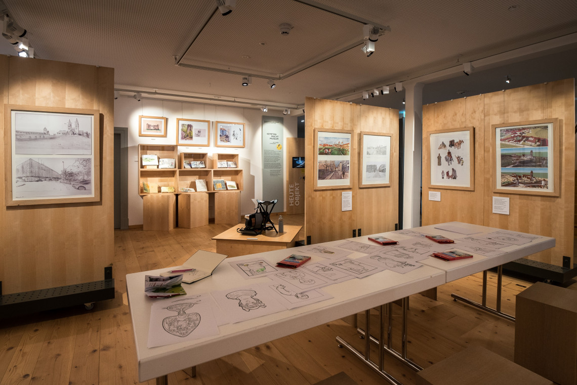 Blick in Ausstellung auf einen Zeichentisch und Zeichnungen an den Wänden