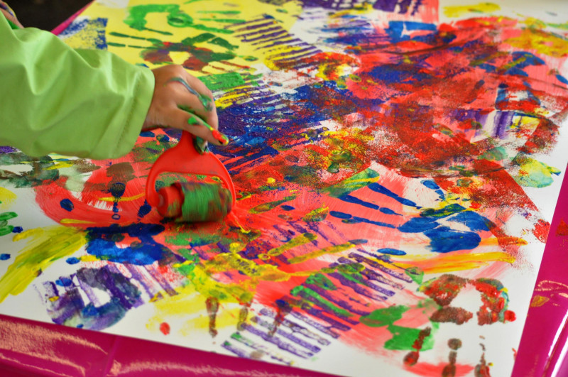 eine Kinderhand f&uuml;hrt eine Farbrolle &uuml;ber ein buntes Papier