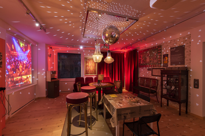 Ausstellungsraum, der wie ein Caf&eacute; eingerichtet ist mit stimmungsvollem roten Licht wie auf einer Tanzfl&auml;che