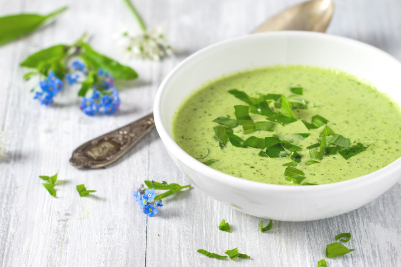 ein weißer Porzellanteller mit grüner Suppe und Suppenlöffel