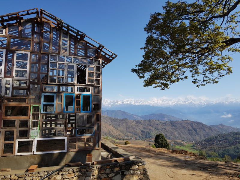 Blick in eine Berglandschaft, im Vordergrund eine Haus, das aus gebrauchten Fenstern gebaut ist